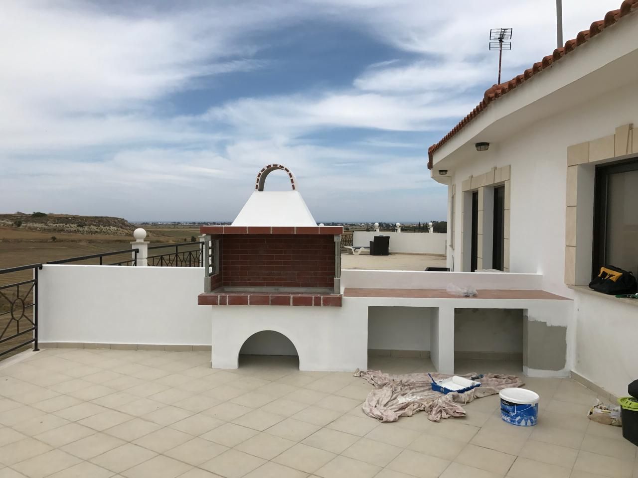 Built-in barbecue rendered white with a tiled counter, with painting in progress on the roof terrace